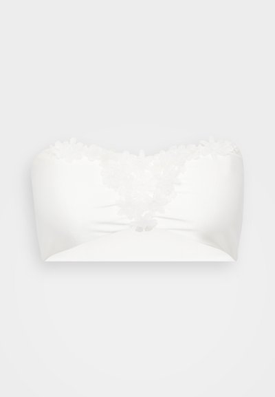 Bandeau blanc sans bretelles avec des appliqués floraux au niveau du décolleté, texture satin lisse et design ajusté.