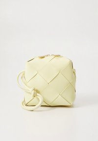 Sac à main tissé jaune de forme carrée, avec des panneaux texturés et une sangle nouée. Le matériau semble être synthétique ou en cuir synthétique.