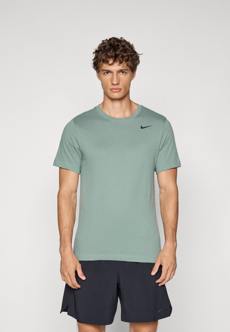 Camiseta de manga corta verde claro hecha de tela suave, con un logotipo negro de Nike en la parte superior izquierda del pecho. Combinada con pantalones cortos oscuros.