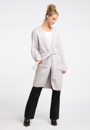 Cardigan lavorato a maglia grigio chiaro con cintura, vestibilità oversize, scollo a V profondo, polsini e orlo a coste, dotato di tasche frontali. Indossato sopra una maglietta bianca.