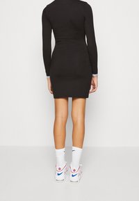 Vestido negro de manga larga con un diseño ajustado, combinado con zapatillas deportivas blancas y rojas y calcetines deportivos blancos. Silueta simple y elegante.