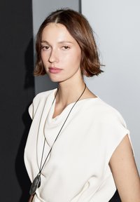 Wit gedrapeerd topje met korte mouwen, zachte textuur, gecombineerd met een lange zwarte koordketting met een slank, ovaal zilveren hangertje.