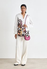 Bílá košile s odvážným květinovým vzorem v růžové a černé barvě, doplněná volnými bílými kalhotami a malou růžovou kabelkou. Ploché boty s černou podrážkou.