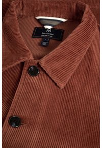 Bruine corduroy jas met zwarte knopen en gestreepte binnenkraag, met een label "Matinique Heritage Apparel" in maat large.