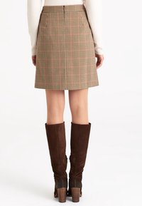 Hnědá kostkovaná sukně s přiléhavým pasem, sahající do poloviny stehen a s plisemi, spárovaná s vysokými hnědými semišovými vysokými botami na podpatku.
