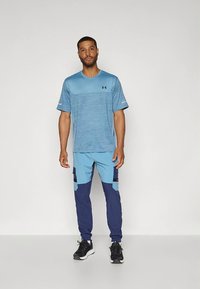 Lichtblauw sportshirt met gestreepte textuur, gecombineerd met blauwe en donkerblauwe cargobroeken met zakken. Zwarte sneakers maken de outfit compleet.