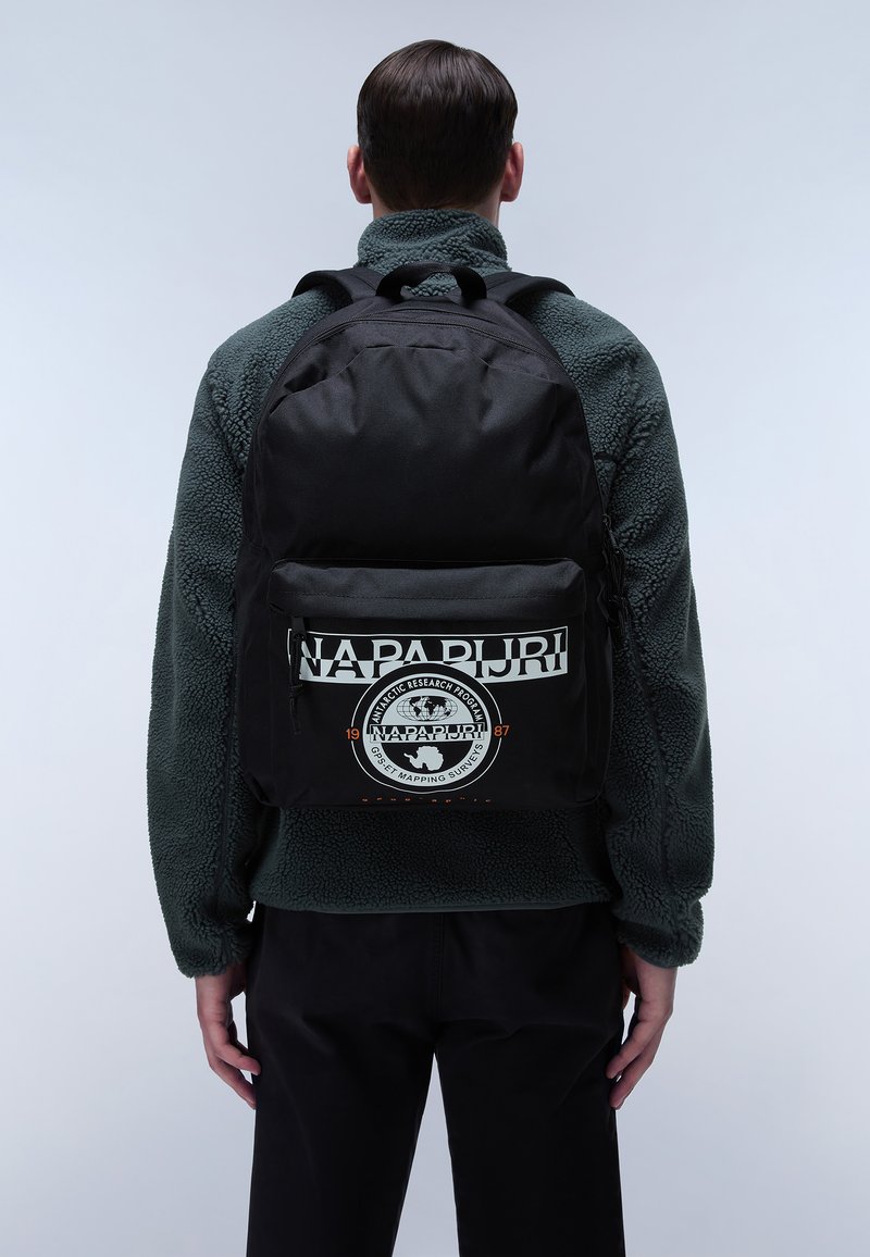 Zaino in tessuto nero con una grande tasca frontale, caratterizzato da un logo circolare e testo. Il design include spallacci regolabili e una texture morbida.
