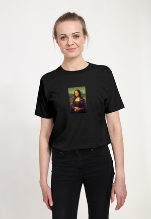Kvinde iført sort t-shirt med tryk af Mona Lisa-malet, stående mod en ensfarvet lys baggrund.