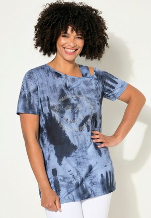 Modré tričko s tie-dye vzorem, krátkými rukávy, výřezem na jednom rameni a designem úsměvné tváře z kamenů uprostřed. Jemný bavlněný materiál.