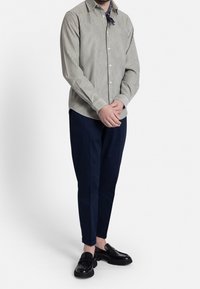 Camisa de botones de rayas en verde claro, de mangas largas. Combinada con pantalones oscuros en navy y mocasines negros. Textura y ajuste notables.