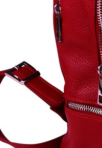 Sac en cuir texturé rouge avec une fermeture éclair en métal, une bandoulière métallique avec une boucle et des détails de couture subtils.