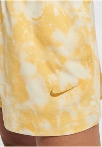 Žlté šortky s tie-dye vzorom vyrobené z bavlnenej tkaniny, so štruktúrovaným vzorom a malým vyšitým zlatým logom Nike na leme.