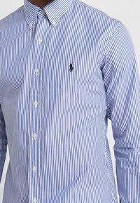 Blå och vit randig button-up skjorta i bomull, med en klassisk krage, framknäppning och en liten logotyp på bröstet.