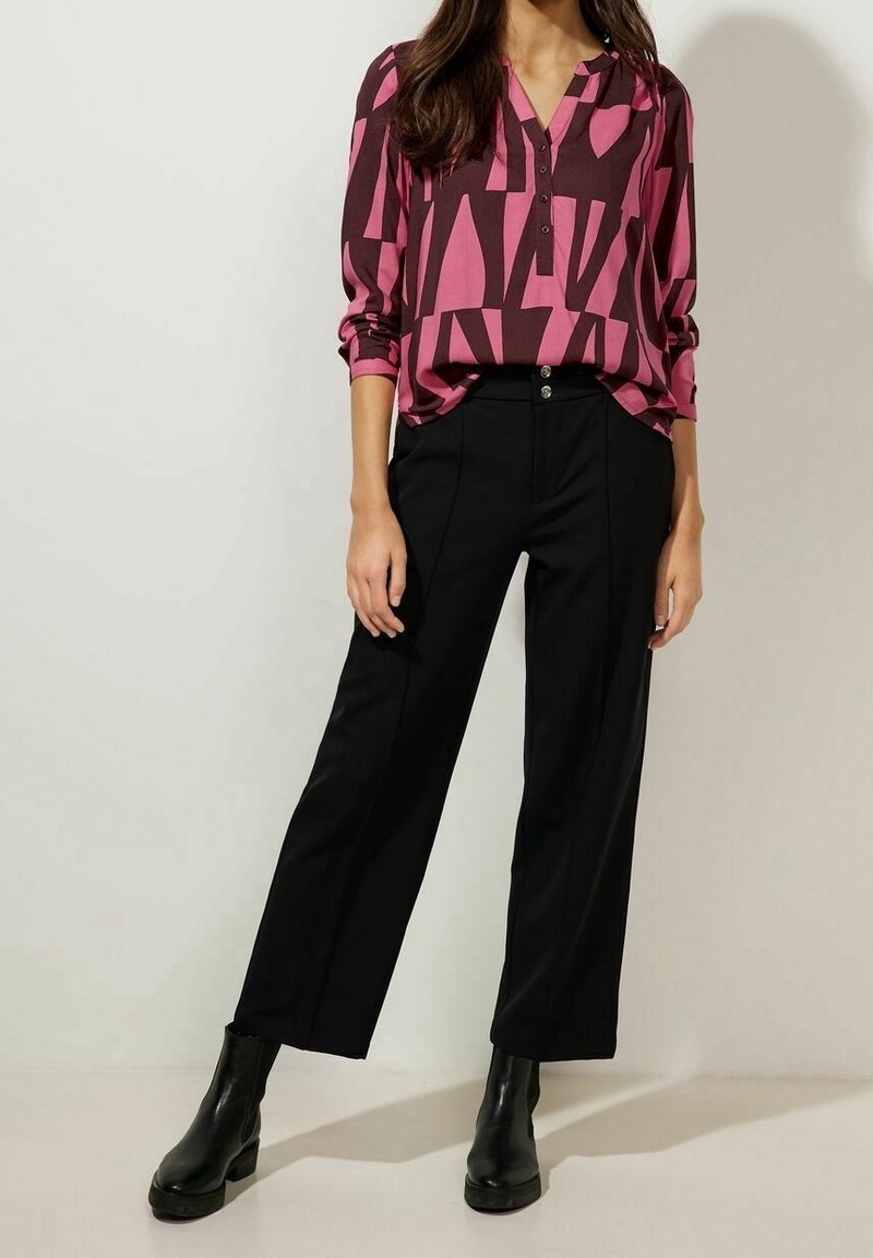 Chemise à manches longues avec un motif géométrique rose et bordeaux, associée à un pantalon noir à jambes larges et des bottines noires, avec un devant à boutons.