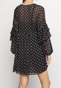 Musta, kuvioitu mekko, joka on valmistettu läpikuultavasta kankaasta, jossa on röyhelöhihoja ja tiukka vartalo. Mekossa on punaisia ja valkoisia timanttikuviota.