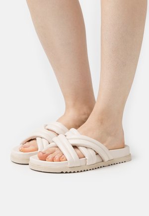 Beige Rutschsandalen mit verflochtenem Riemendesign, weichem Material, flacher Sohle und strukturiertem Außensohlen für besseren Halt. Sichtbare Zehen.