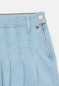Shorts in denim bluastro con design plissettato, tasca con zip e etichetta con logo in rosso, bianco e blu sulla vita.
