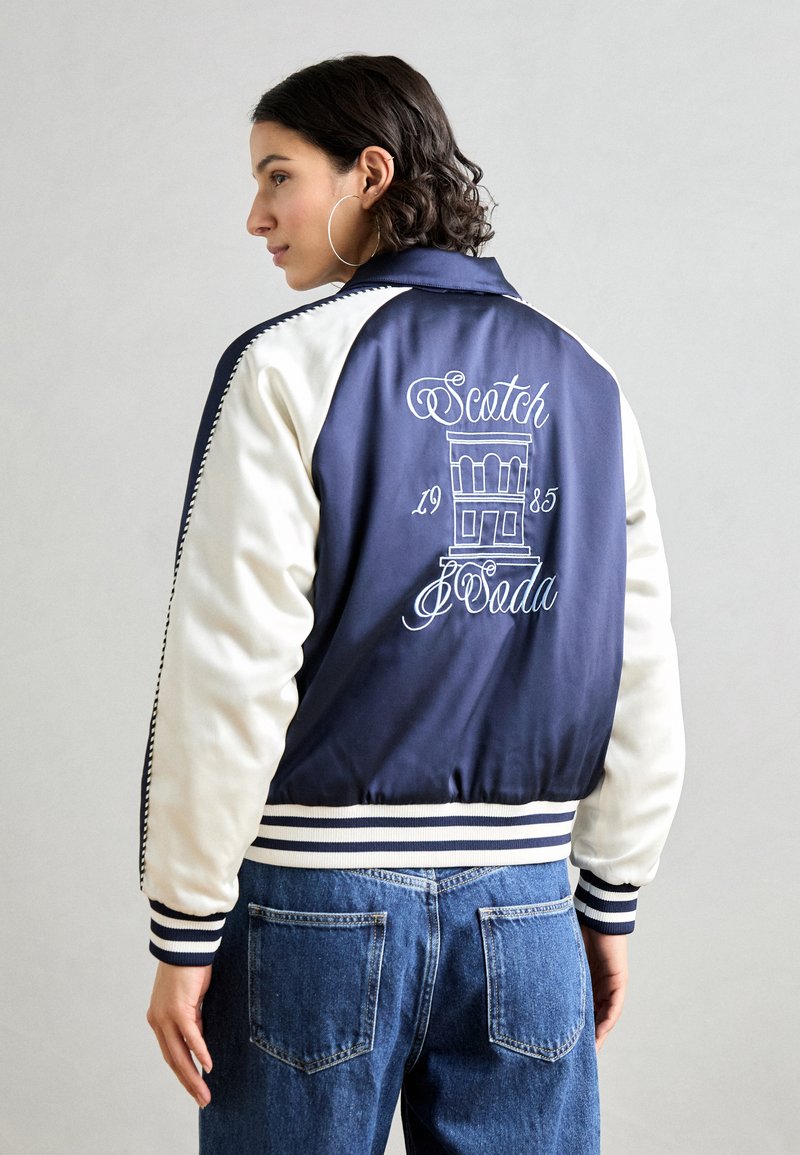 Tengeréskék és fehér bomber dzseki bordázott mandzsettákkal, hímzett "Scotch & Soda" logóval és grafikai dizájnnal a háton. Puha, sima anyag.