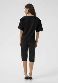 T-shirt noir surdimensionné à manches courtes, texture douce et encolure large, associé à un pantalon noir court et des talons noirs.