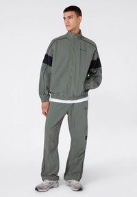 Sportowa kurtka i spodnie w jasnym zielonym kolorze z czarnymi akcentami. Wykonane z gładkiego, lekkiego materiału, z zamkiem błyskawicznym i elastycznymi mankietami.
