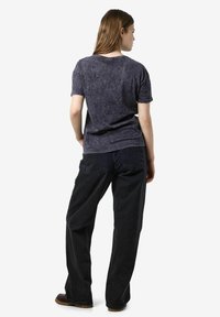 Korte mouwen donkergrijze T-shirt met een zachte, gestructureerde oppervlakte, gecombineerd met losse zwarte jeans en bruine schoenen. Opgerolde mouwen detail zichtbaar.