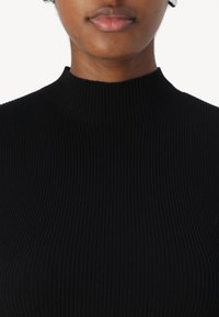 Haut noir à col montant en maille côtelée, fabriqué à partir d'un tissu extensible, présentant des lignes verticales et une silhouette ajustée. Pas d'ornements supplémentaires.