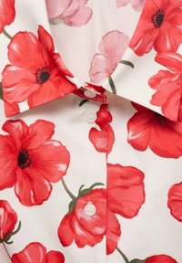 Chemise blanche à col avec motif de fleurs de coquelicot rouges et boutons blancs visibles sur le devant.