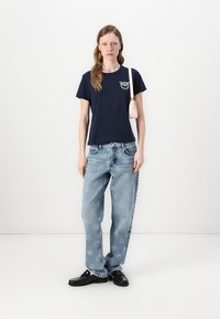 T-shirt di cotone navy con una piccola stampa grafica, abbinato a jeans azzurri a vestibilità ampia con motivi floreali e scarpe nere.