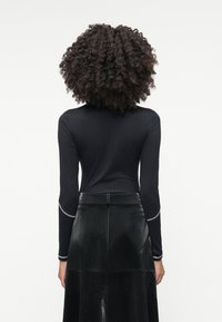 Blusa preta de mangas longas com uma textura suave, apresentando um detalhe prateado em contraste nos punhos. Combinada com uma saia de pele sintética preta.