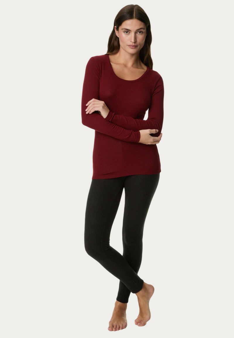 Bordeaux langmouwen top van ribbelstof, gecombineerd met zwarte leggings. De top heeft een ronde hals en een aansluitende pasvorm.