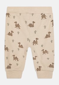 Beige ribbade babybyxor med tryck av kamel och kaktus. Har elastisk midja och åtsittande mudd. Mjuk textur, varmt tyg.