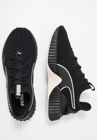 Zwarte sportieve schoenen met een geweven bovenwerk met textuur, een dikke witte middenzool en een zwarte rubberen buitenzool. Voorzien van veters en logo-accenten.
