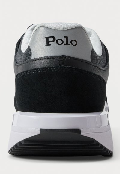 Achteraanzicht van een zwart-grijze sneaker met een witte zool, met "Polo" branding op de hielkraag.