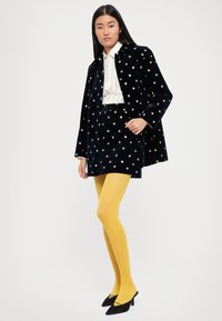 Granatowy aksamitny płaszcz z kwiatowym haftem, zestawiony z białą strukturalną bluzką, granatową spódnicą, jasnoniebieskimi rajstopami i czarnymi szpilkami.