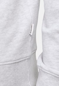 Felpa grigia in morbido cotone, con polsini a costine e un'etichetta laterale con la scritta "JACK & JONES" stampata. Visibili dettagli nella cucitura e nella texture.