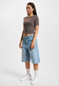 Brown cropped T-shirt, light blue denim bermuda shorts with frayed hem, white sneakers, and white athletic socks. Simple design and fit.