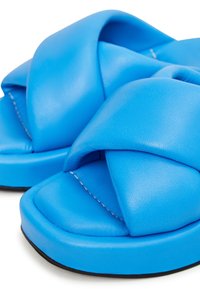 Modré sandály z umělé kůže s křížovým designem, polstrovanými popruhy a měkkou podrážkou s černou gumovou spodní částí.