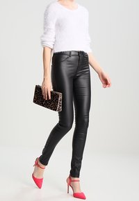 Pantaloni in finta pelle nera con una vestibilità slim, abbinati a un morbido maglione bianco e tacchi alti rosa. Gli accessori includono una pochette con stampa leopardo.