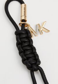 Porte-clés en cuir noir avec une texture tressée, présentant un charm "MK" doré et un élément de quincaillerie doré cylindrique gravé de "Michael Kors".
