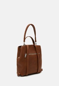 Bolso de cuero marrón con asa trenzada en la parte superior, correas de hombro ajustables y bolsillo con cremallera plateada en el frente, sobre fondo blanco.