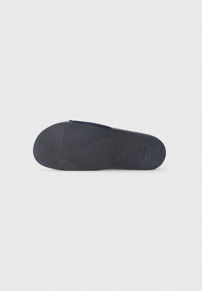 Semelle de chaussure en caoutchouc noir avec un motif hexagonal et une surface texturée pour une meilleure adhérence. Présente un design plat avec une légère courbure.