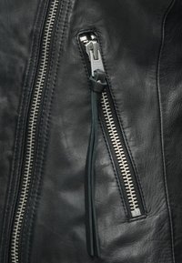 Czarna skórzana kurtka w zbliżeniu, z metalowymi zamkami błyskawicznymi, teksturowaną powierzchnią oraz skórzanym uchwytem suwaka o subtelnym połysku.