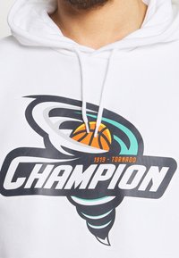 Vit hoodie med en stor grafik av en tornado och en basketboll, med fettexten "CHAMPION" i svart, teal och orange akcentfärger.