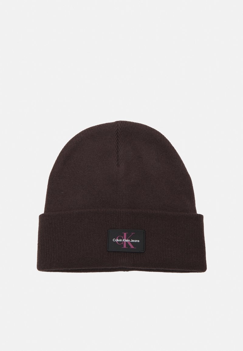 Bonnet en maille brun foncé avec revers comportant un patch noir rectangulaire marqué "Calvin Klein Jeans" en texte blanc et rouge.