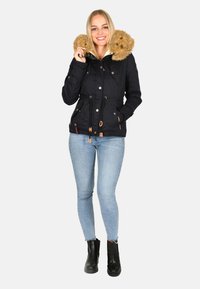 Marineblaue isolierte Jacke mit einer mit Fleece gefütterten Kapuze, Kordelzug in der Taille und Knopfakzenten. Getragen zu hellblauen Jeans und schwarzen Ankle Boots.