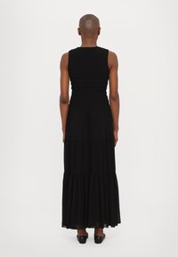 Rochie maxi neagră, cu un corset ajustat din smocă, design fără mâneci și fustă fluida, în straturi. Pantofii negri, lucioși, completează ținuta.