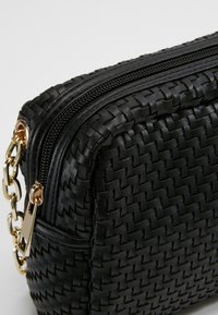 Sac en cuir tressé noir avec une finition texturée, fermeture éclair et quincaillerie dorée. Équipé d'une attache pour une chaîne sur le côté.