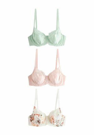 Žena so svetlými vlasmi, ktorá nosí kvetinový čipkovaný podprsenku a nohavičky s vysokým pásom, pózuje s jednou rukou na bedrách na jednoduchom pozadí.