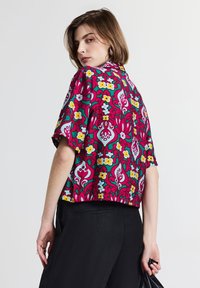 Top corto, a maniche corte, con un design boxy che presenta un vivace motivo floreale in rosa, verde e bianco su uno sfondo blu. Tessuto leggero con vestibilità comoda.