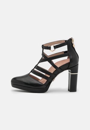Chaussure à talons hauts en cuir noir avec un design de sangle découpée, bout rond et talon bloc. Présente un accent en ton doré et une fermeture éclair.